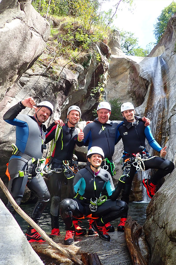 Gruppe von Teilnehmern beim Canyoning in Cresciano im Boggera-Canyon – lachend vor Wasserfall mit Ausrüstung und purelements®-Helmen
