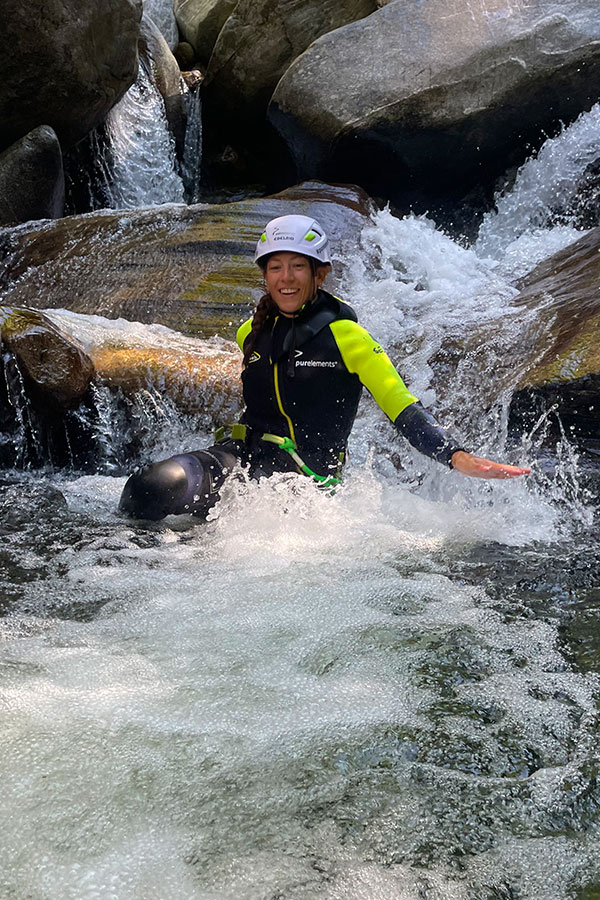 Teilnehmerin rutscht lachend eine natürliche Wasserrinne im Val Grande Canyon hinunter – Canyoning mit purelements® im Tessin