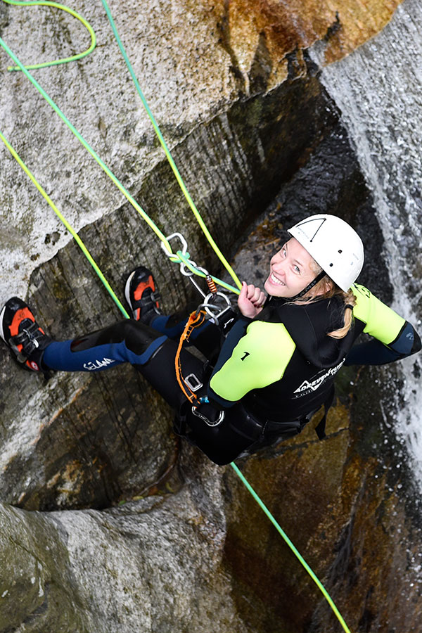 Lächelnde Frau seilt sich Wasserfall ab – purelements Abenteuerurlaub Schweiz