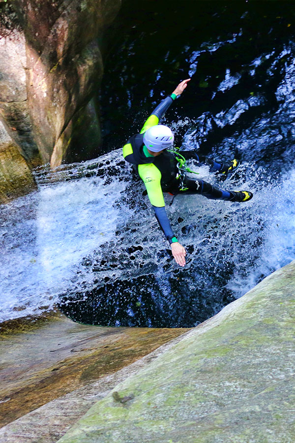 Person rutscht im Corippo Canyon durch eine Felsrinne ins Wasser – purelements Tour für Einsteiger