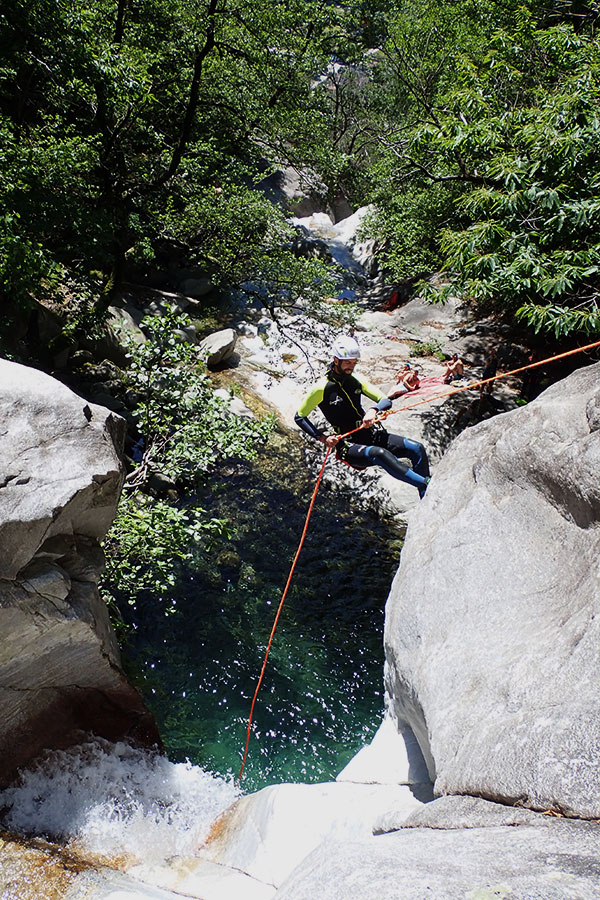 Teilnehmer beim Canyoning im Tessin seilt sich über eine Felswand in ein natürliches Becken mit klarem Wasser ab