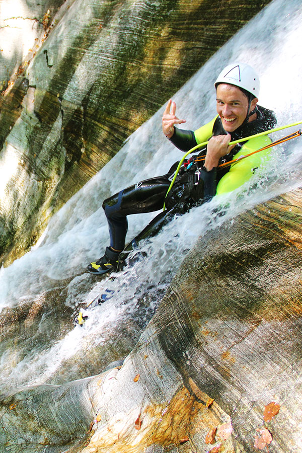 Mann beim Canyoning im Tessin rutscht eine Felsrinne hinunter – purelements® Abenteuer in nachhaltiger Natur